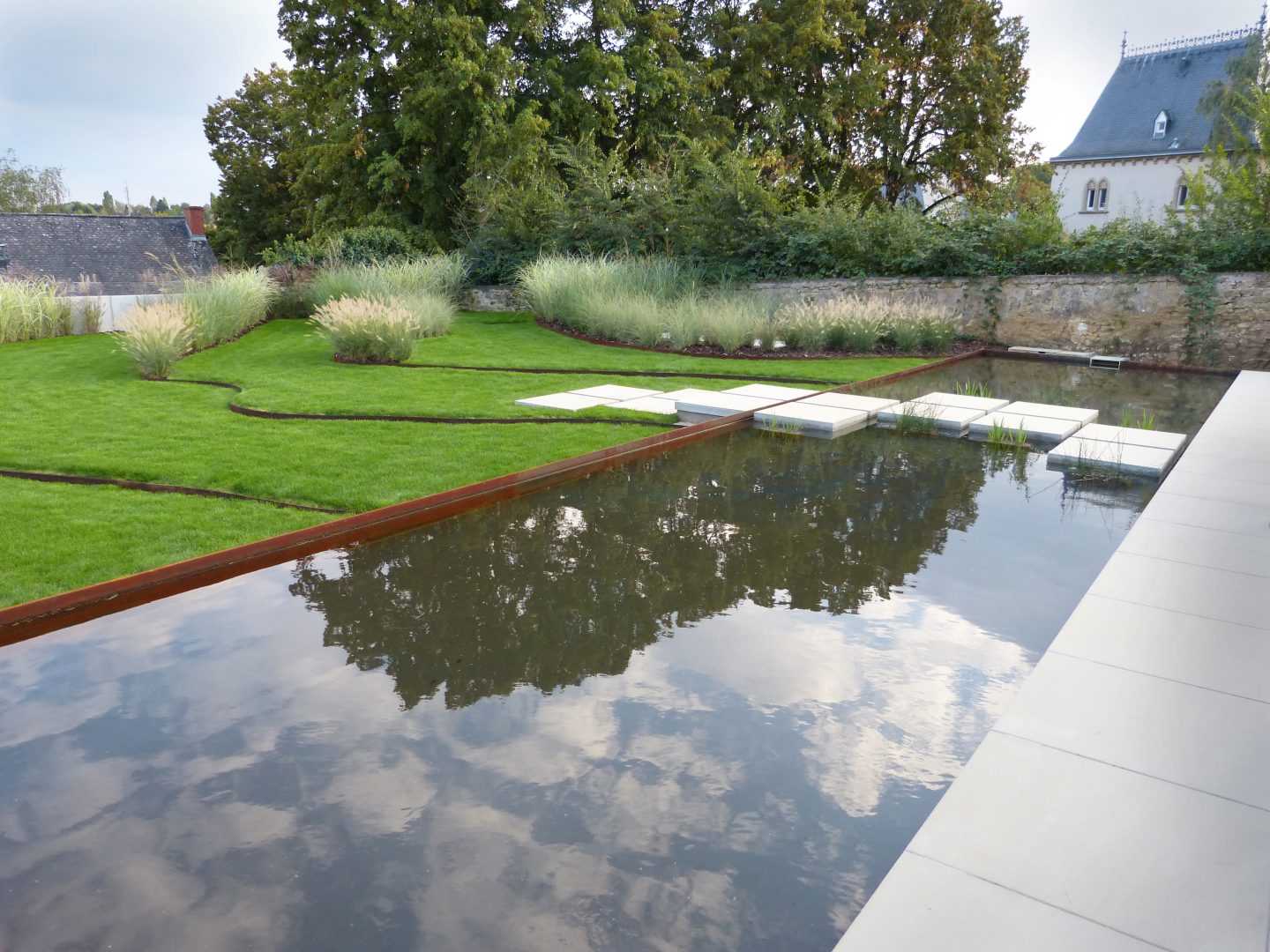 Das Bild zeigt die hellen Steinplatten, die über einen Wasserlauf führen. Wolken spiegeln sich im Wasser.