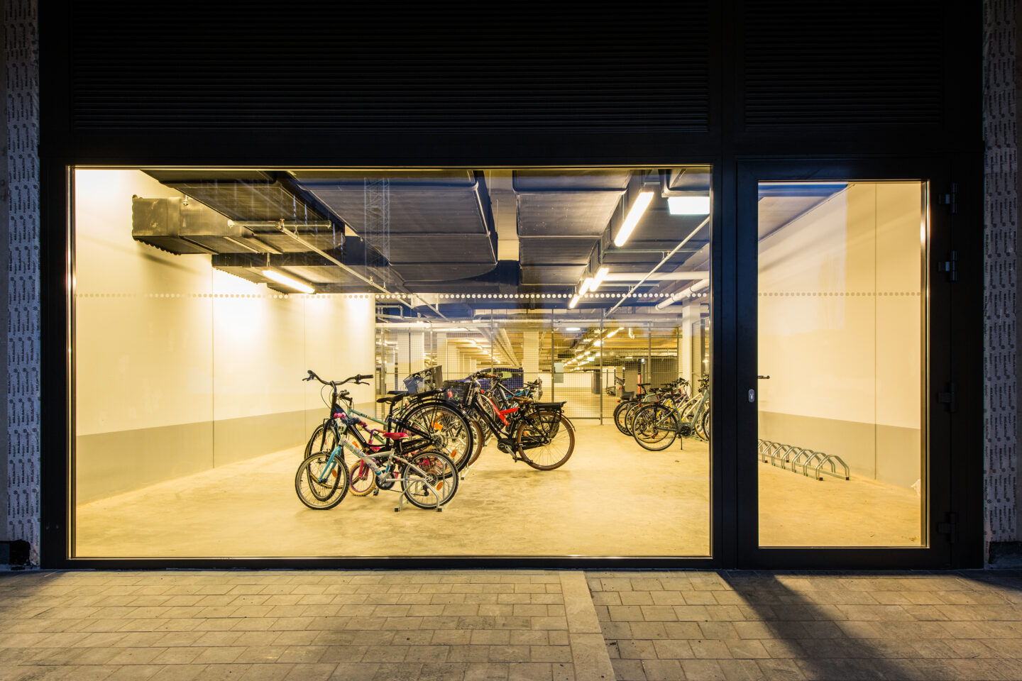 Ein Blick durch den beleuchteten Fahrradkeller in die Tiefgarage